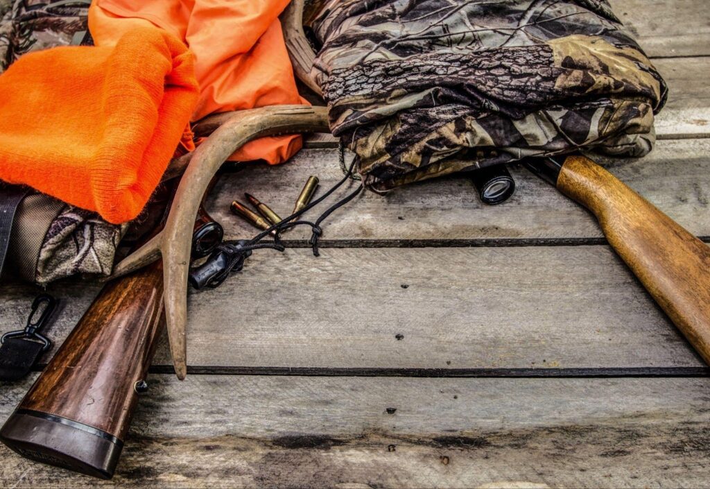 Various hunting items, such as a backpack and binoculars laid out on a wooden floor surface